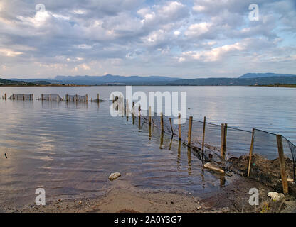 Poteaux de bois avec grillage de séparation métallique dans la mer de Gialova lagune, Péloponnèse, Grèce. Ciel nuageux au-dessus de la mer spectaculaire rippled water surface. Banque D'Images