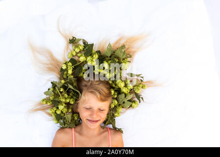 Portrait de l'adorable petite fille couchée sur fond blanc avec le houblon vert stylisé en plante sèche Banque D'Images