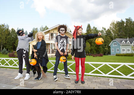 Groupe multi-ethnique des enfants portant des costumes de Halloween posant en rue tout en tour ou traitement, copy space Banque D'Images
