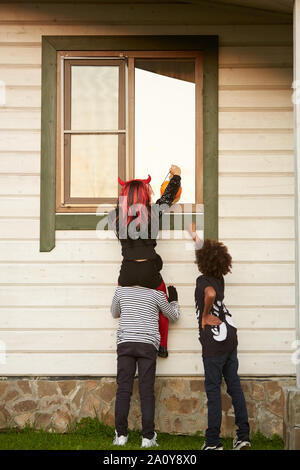 Vue arrière de la fenêtre de l'escalade enfants sournois chambre tandis que trick or treating dans Halloween, copy space Banque D'Images