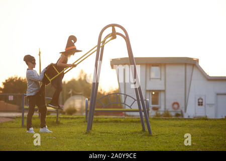 Vue latérale du portrait des enfants jouant dehors teenage boy poussant girl having fun on swing, copy space Banque D'Images