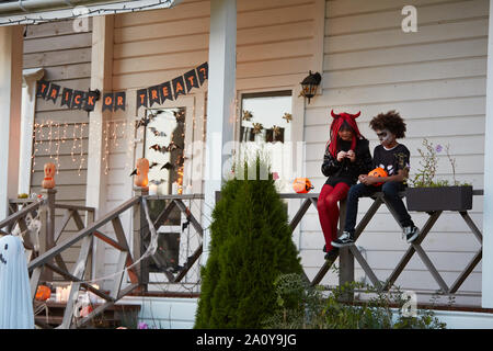 Vue grand angle au garçon et fille Halloween manger assis sur la clôture après le tour ou les traiter ensemble, copy space Banque D'Images