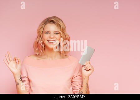 Jeune étudiant hipster femme avec des poils de couleur et de tatouage holding passport sur le fond rose. Studio. Voyage Concept Banque D'Images