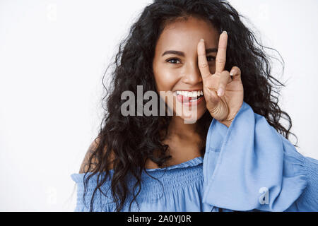 Close-up et coquettes, ludiques féminin afro-américain aux cheveux bouclés en blouse bleu femelle stupide, montrant la langue, faire la paix, la bonne volonté de signer plus de fa Banque D'Images