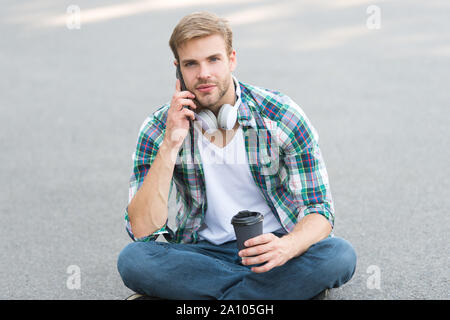 Appel important. appel téléphonique. écouter la musique. ebook concept. homme Chemise à carreaux. élève se détendre et recharger. café d'aller. guy boire un café en plein air. L'homme s'asseoir sur le sol. étudiant insouciant en casque. Banque D'Images