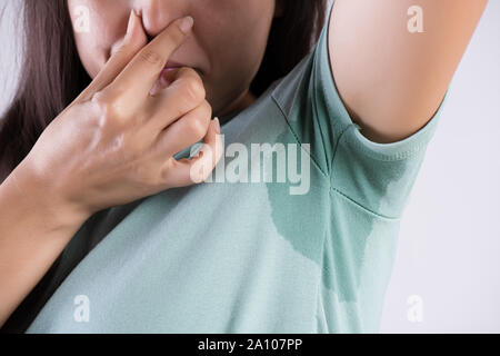 Gros plan femme asiatique avec l'hyperhidrose la transpiration. Jeune femme d'Asie de sueur tache sur ses vêtements contre un arrière-plan gris. Concept de soins de santé. Banque D'Images