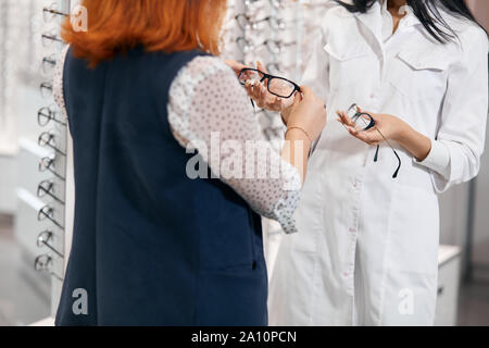 Jeune femme en blanc manteau de donner des conseils médicaux d'acheter nouveau modèle de eyewears, Close up photo recadrée. Banque D'Images