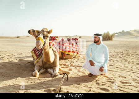 Homme portant des vêtements traditionnels, en tenant un chameau sur le sable du désert, à Dubaï Banque D'Images