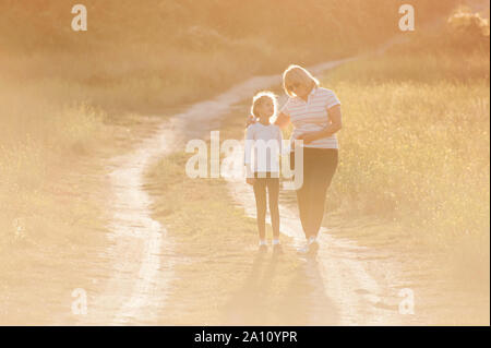 Famille heureuse grand-mère fat woman hugging peu mince petite fille au cours de loisirs en plein air, l'activité sportive d'un rétro-éclairage par le coucher du soleil avec copyspace Banque D'Images