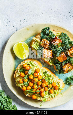 Les sandwiches ouverts vegan avec guacamole, le tofu, les pois chiches et les graines germées dans une assiette. La nourriture végétalienne saine concept. Banque D'Images
