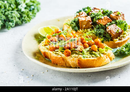 Les sandwiches ouverts vegan avec guacamole, le tofu, les pois chiches et les graines germées dans une assiette. La nourriture végétalienne saine concept. Banque D'Images