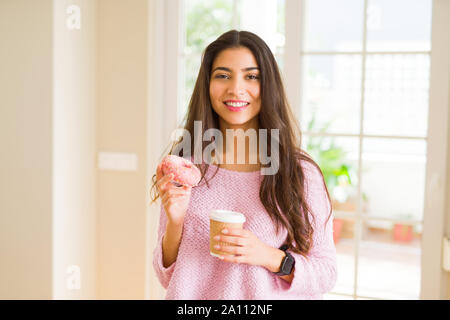 Jeune travailleur woman eating donut rose savoureux et de boire une tasse de café Banque D'Images