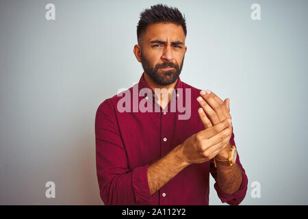 Jeune Indien man wearing red shirt debout sur fond gris isolés souffrant de douleur sur les mains et les doigts, l'inflammation de l'arthrite Banque D'Images