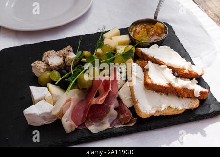 La plaque avec un assortiment de fromages, olives, Parshuto, toasts et confiture. Snack de vin sur une nappe de coton blanc dans un café. Banque D'Images