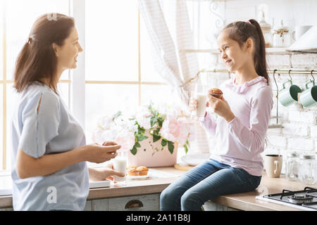 Petite fille de manger des collations et bavardant avec maman dans la cuisine Banque D'Images