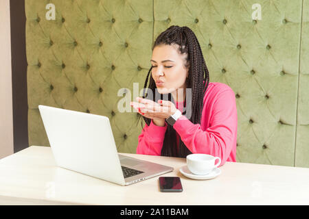 Portrait d'une belle jeune fille romantique indépendant avec des dreadlocks hairstyle en chemisier rose sont assis tout seul, faisant appel vidéo ou vlog à Banque D'Images