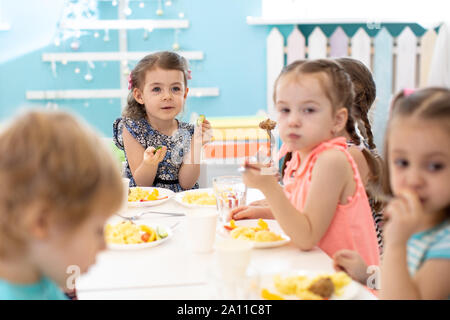 Groupe d'enfants assis à la table avec déjeuner et manger appétissants. Les enfants ont un dîner à la maternelle ou à la garderie Banque D'Images