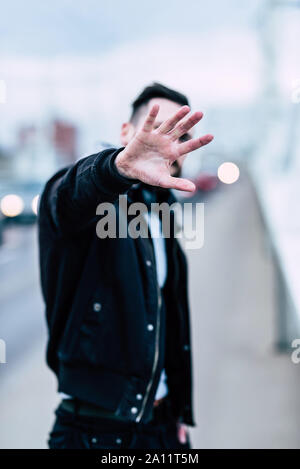 Un jeune homme hipster couvrant son visage avec sa main dans un environnement urbain. Banque D'Images