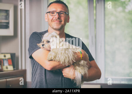 Homme tenant un mignon petit chien maltais blanc sur son épaule à la maison Banque D'Images