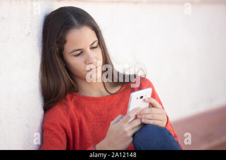 Chica adolescente feliz mirando el sentada smartphone en la azotea Banque D'Images
