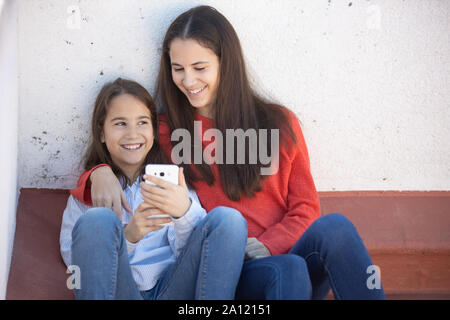 Dos Hermanas mirando el smarthphone sentadas en la azotea Banque D'Images