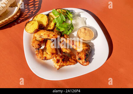 Ailes de poulet frites sur une assiette avec une salade de pommes de terre et d'herbes fraîches sur la table rouge. close up Banque D'Images