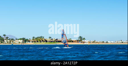 Windsurfer en mer sur l'arrière-plan de la plage avec des palmiers et de hautes montagnes rocheuses en Egypte Dahab Banque D'Images