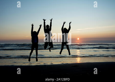 Trois Silhouettes d'teanagers sautant joyeusement sur la plage avec un coucher de soleil à l'bakcground Banque D'Images