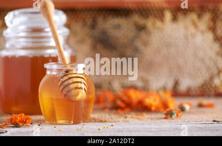 Miel de fines herbes en pot avec balancier, miel, pollen d'abeille en granulés, le calendula fleurs sur fond gris Banque D'Images