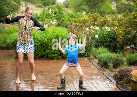 Garçon de 5 ans et sa soeur de 13 ans la danse de la pluie. Banque D'Images