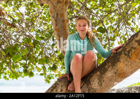 Une jeune fille assise dans un arbre en riant. Banque D'Images