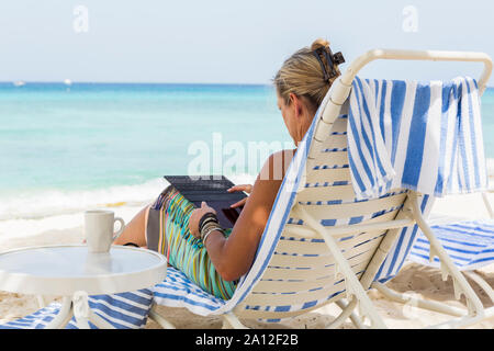 Femme adulte conseil d'utilisation de smart phone sur la plage, l'île Grand Cayman Banque D'Images