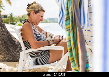 Femme adulte conseil d'utilisation de smart phone sur la plage, l'île Grand Cayman Banque D'Images