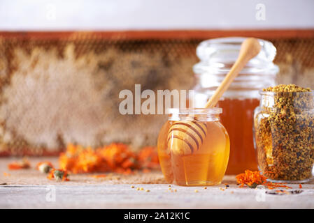 Miel de fines herbes en pot avec balancier, miel, pollen d'abeille en granulés, le calendula fleurs sur fond gris Banque D'Images