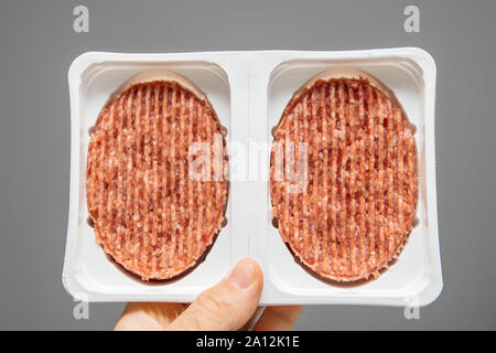 Man main holding fresh steak escalopes dans les bénéficiaires de l'aide de plastique blanc fond gris Banque D'Images