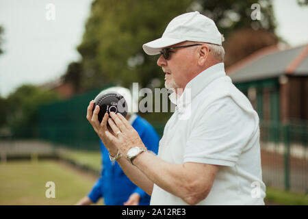 Un gros plan d'un senior man holding a boules lyonnaises, prêt à prendre sa photo. Il porte un capuchon blanc et lunettes de soleil. Banque D'Images