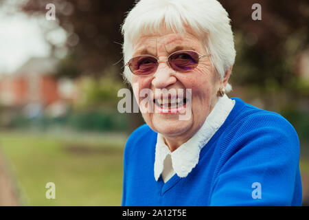 Un gros plan d'un senior woman smiling, regardant la caméra. Elle porte des lunettes de couleur rose. Banque D'Images