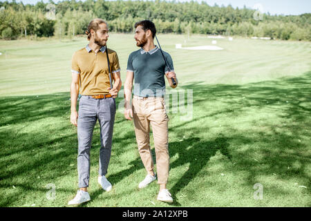 Deux meilleurs amis masculins à marcher avec le matériel de golf sur le magnifique parcours de jeu, parler et s'amuser lors d'un jeu sur une journée ensoleillée Banque D'Images