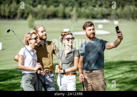 Groupe de jeunes et professionnels amis debout photo selfies avec golf putters au cours d'une partie sur le terrain de golf Banque D'Images