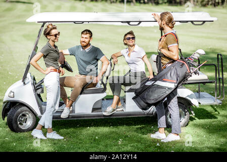 Un groupe de jeunes amis avec équipement de golf près de la voiture de golf sur le cours de jeu avant le jeu Banque D'Images