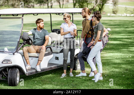 Un groupe de jeunes amis avec équipement de golf près de la voiture de golf sur le cours de jeu avant le jeu Banque D'Images