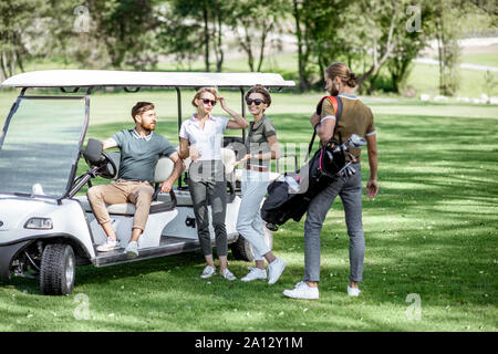 Un groupe de jeunes amis avec équipement de golf près de la voiture de golf sur le cours de jeu avant le jeu Banque D'Images