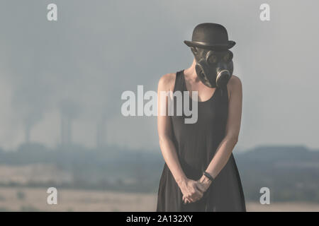 Jeune fille dans une robe noire et un masque à gaz sur l'arrière-plan du tabagisme les cheminées close up Banque D'Images