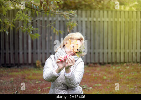 Beautiful happy young woman in park à l'automne la tenue des feuilles. Cheerful blonde woman outdoors in autumn, allongé sur le sol. moyen retoucher. Banque D'Images