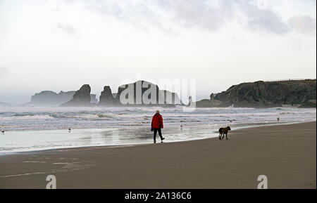 Une femme promener son chien sur la plage au lever du soleil près de Bandon, Oregon.