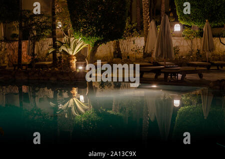 Charm el-Cheikh, Égypte - 0206 2018 : nuit à l'hôtel aquamarine pool vide pliée parasols transats en bois palmiers et arbres décoratifs lant Banque D'Images