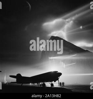 Un Dakota avion du passager qui se profile par projecteurs du rocher de Gibraltar. Banque D'Images