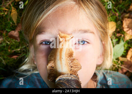 Portrait de la préadolescence adorable enfant fille jouant avec son animal géant de l'escargot africain (Achatina fulica). Escargot rampant sur le visage. Banque D'Images