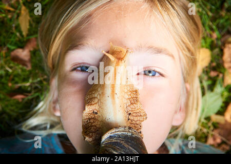 Portrait de la préadolescence adorable enfant fille jouant avec son animal géant de l'escargot africain (Achatina fulica). Escargot rampant sur le visage. Banque D'Images