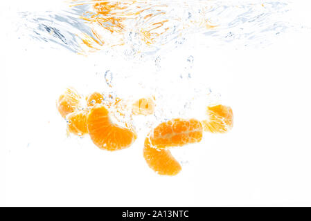 La baisse isolée d'orange dans l'eau. Morceaux de fruits orange pelées dans l'eau isolé sur fond blanc Banque D'Images